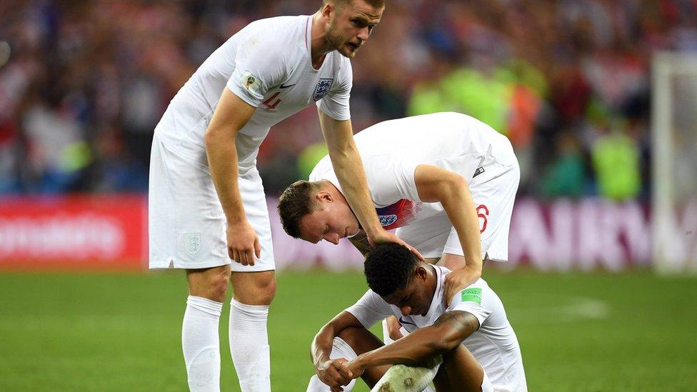 Marcus Rashford is sat on the pitch being comforted by two of his team mates