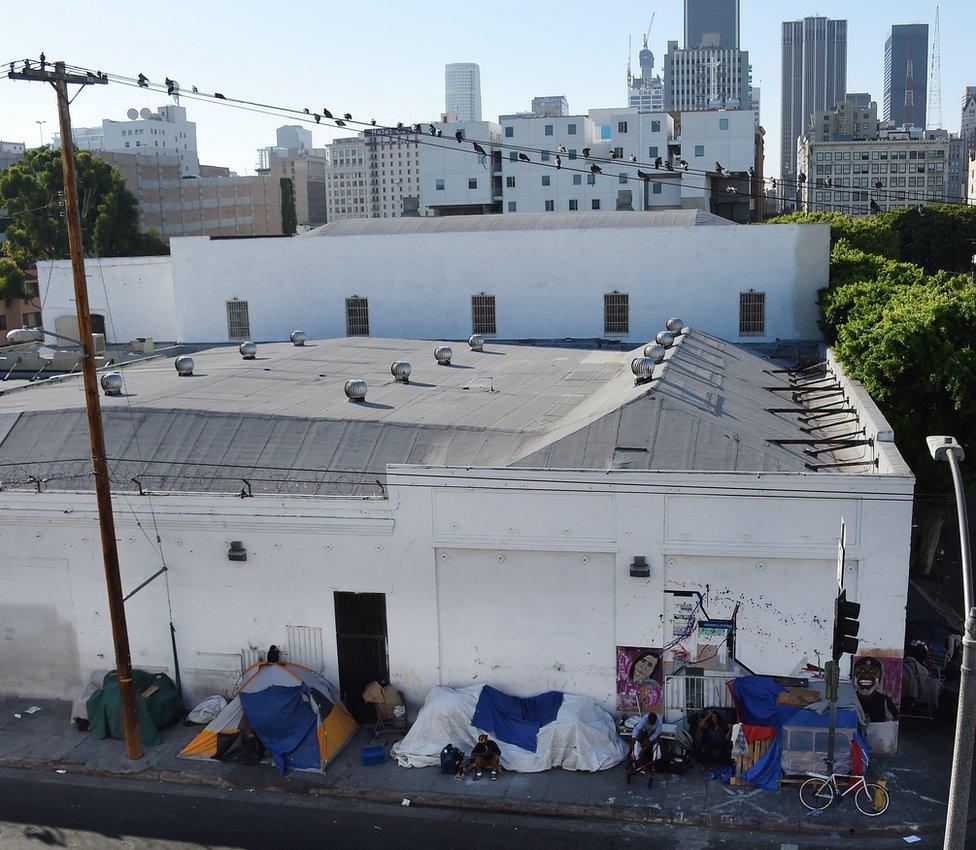 People ride bicycles past tents on Skid Row with the financial district of Los Angles, California, in the background, September 23, 2015