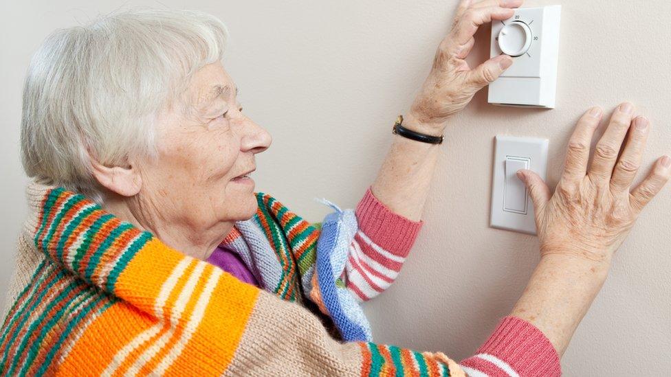 elderly woman adjusts thermostat