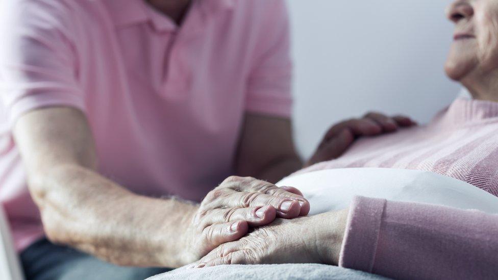 Older couple - with one placing hand on woman's who is lying down