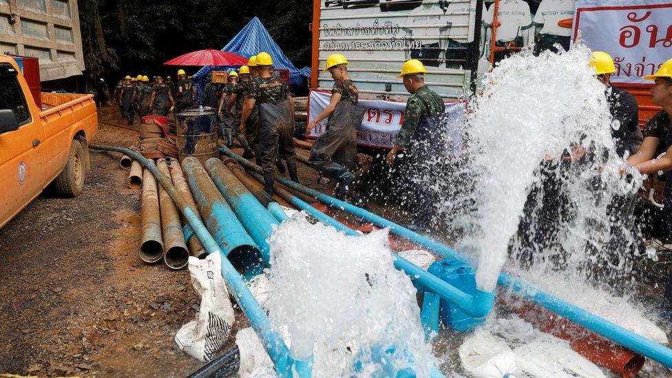 Soldiers and rescue workers walk past water pumped out of Tham Luang cave complex