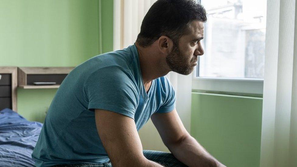 A stock image of a man sitting on the edge of a bed