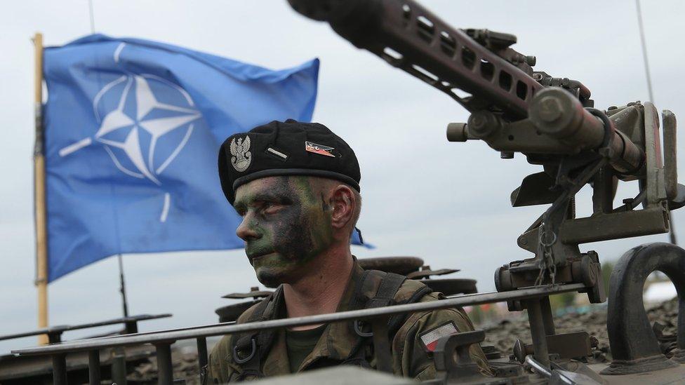 A Polish soldier sits in a tank as a Nato flag flies behind during Nato military exercises on 18 June 2015 in Zagan, Poland