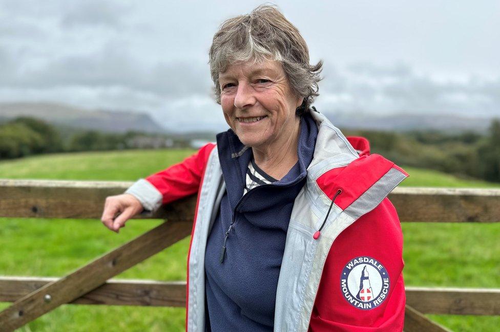 A woman in a red mountain rescue jacket smiles at the camera