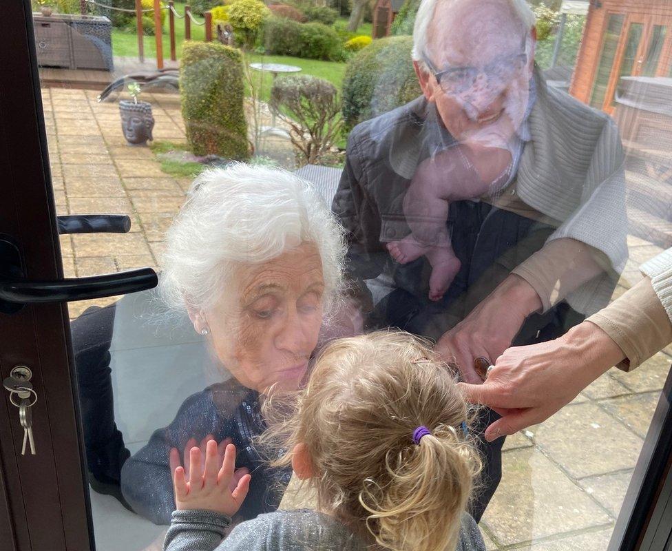 The grandparents kissing their great-grandchildren through the glass