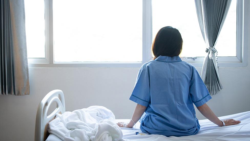 Woman in pyjamas sits on hospital bed, back of head