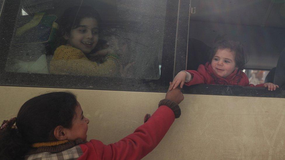 A girl shakes hand with a friend sitting in a bus during the second day of medical evacuations from the besieged rebel-held Eastern Ghouta (14 March 2018)