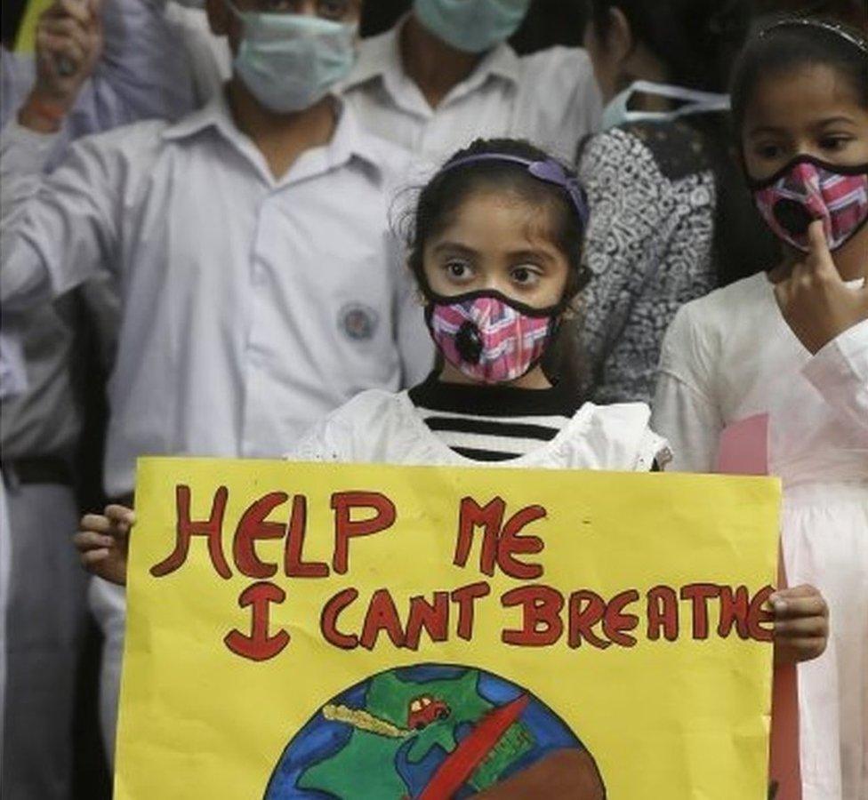 Holding a poster, a girl wears wearing a face mask during a protest against air pollution in New Delhi, India, Sunday, Nov. 6, 2016.