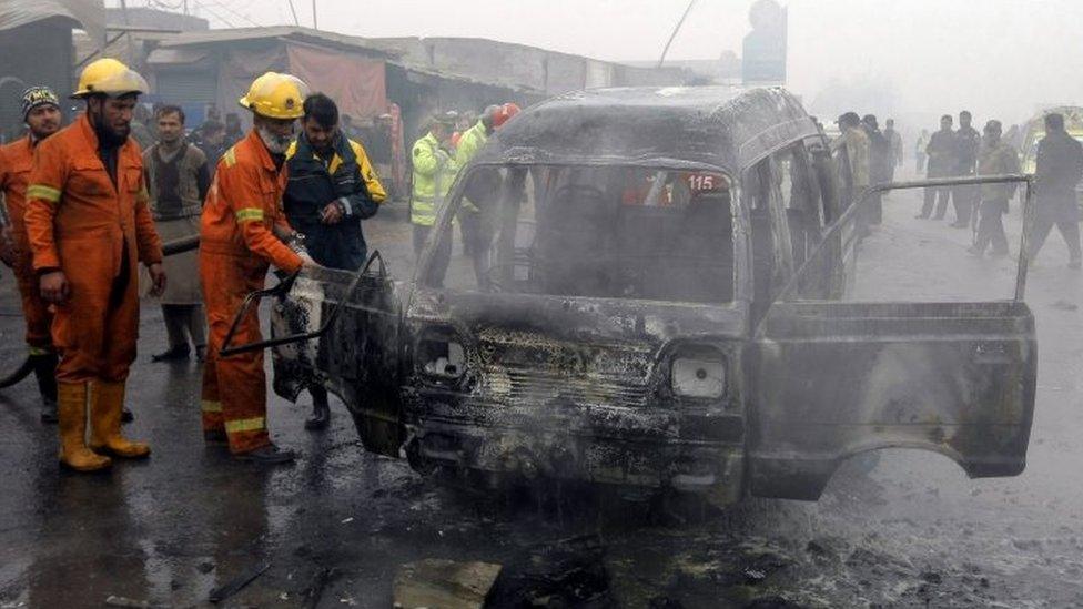 Pakistani fire fighters extinguish the wreckage of a vehicle after a suicide bomb attack on the outskirts of Peshawar (19 January 2016)