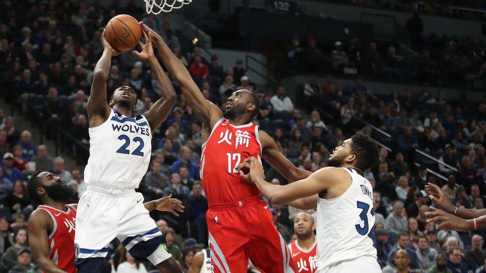 Basketball players struggle over the ball below a basket.