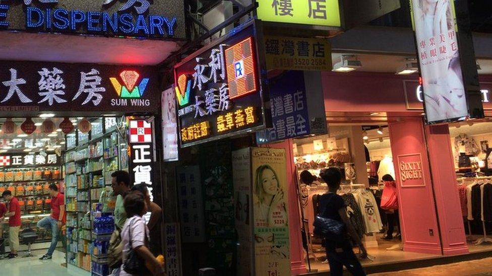 The bookshop is marked by a small blue sign, sandwiched between shops selling vitamins and clothing