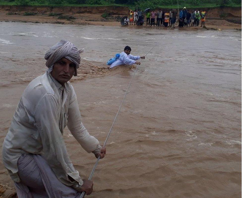 This photo taken on July 25, 2017 shows Indian men trying to cross flood waters in Deesa municipality, which has been hit by severe flooding along the Banas River in northern Gujarat state in western India