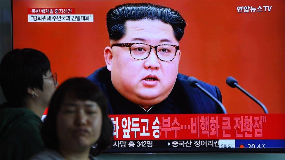 People at a train station in Seoul walk past a television screen showing footage of Kim Jong Un