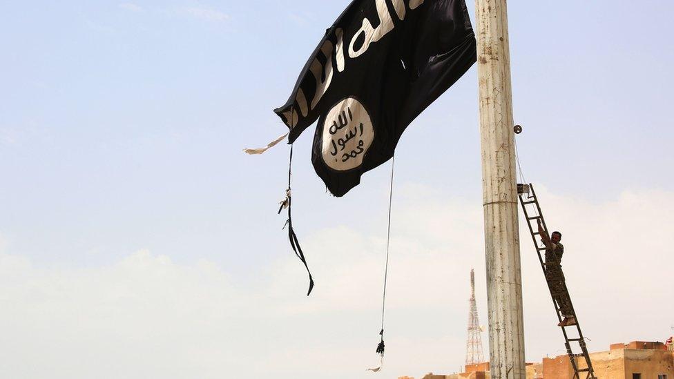 A Syrian Kurdish fighter takes down an IS flag in the town of Tabqa (30 April 2017)