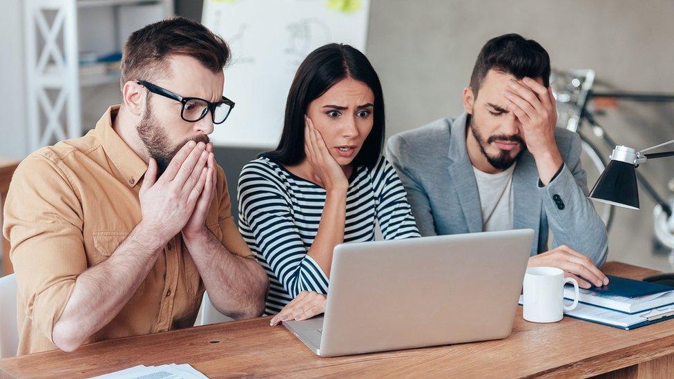 Three people in front of a laptop looking unhappy