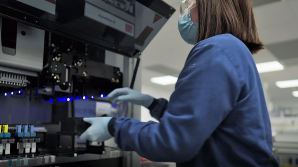 A person in a face covering and latex gloves handles DNA samples in a laboratory