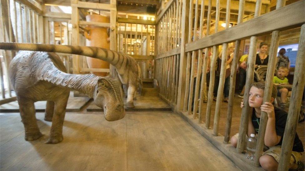 A visitor looks into a cage containing a model dinosaur inside a replica Noah's Ark at the Ark Encounter theme park