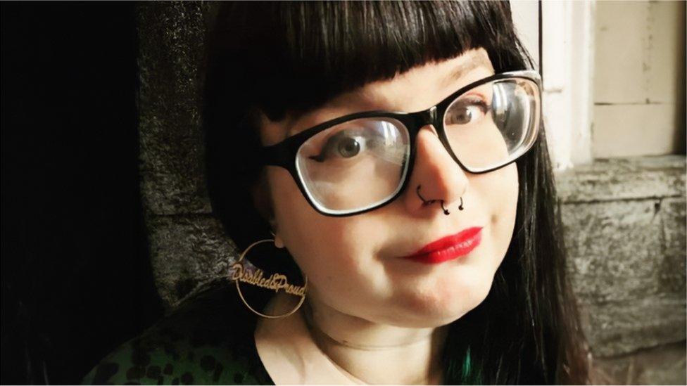 Abi wearing black-rimmed glasses and red lipstick and 'disabled and proud' earrings