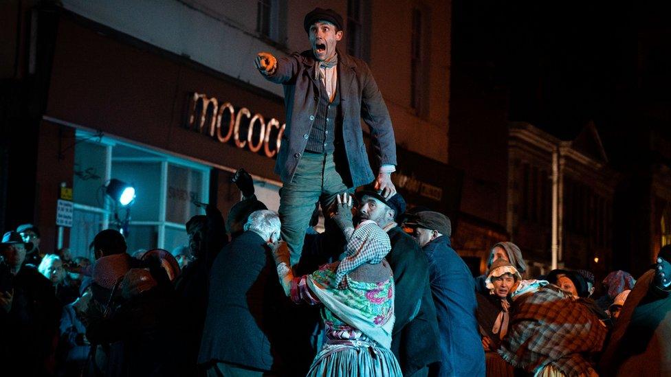 A scene from a Theatr Clwyd street production depicting the 1869 Mold Riots - a man held aloft, pointing and shouting