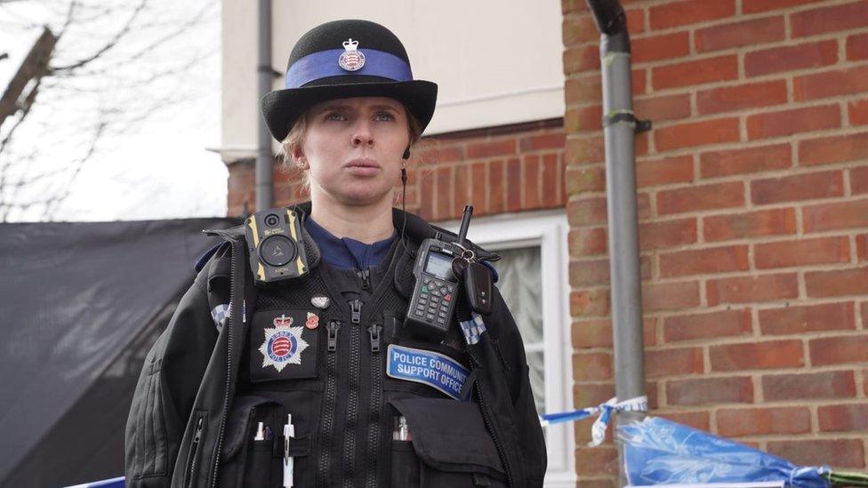 A police community support officer stands in front of a cordoned-off property