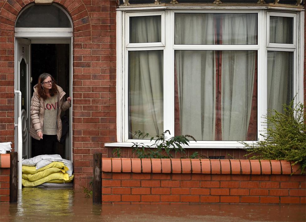 A woman stands with sandbags outside her house