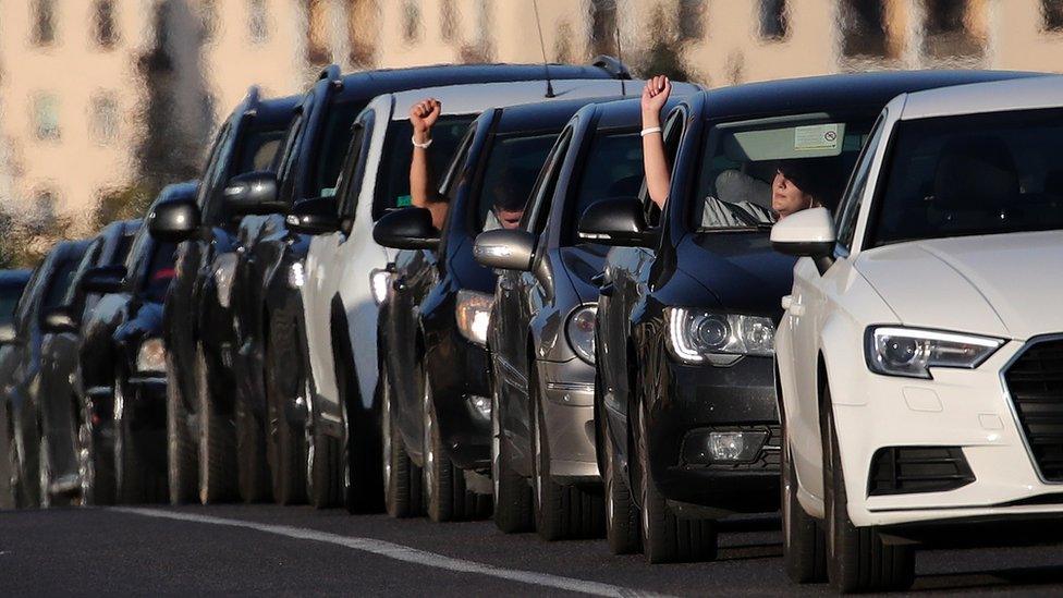 People in cars honk and show their hands with white ribbons - symbols of the protests - on their wrist