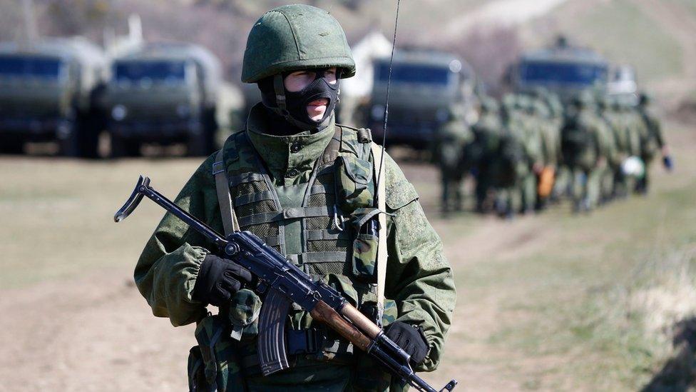 An armed man, believed to be a Russian soldier, stands on guard outside a military base in Perevalnoye