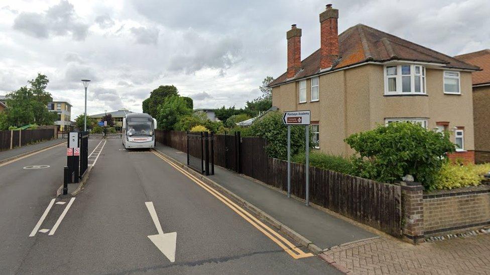 Entrance to school showing direction arrows, gates, and a bus by the side of the road