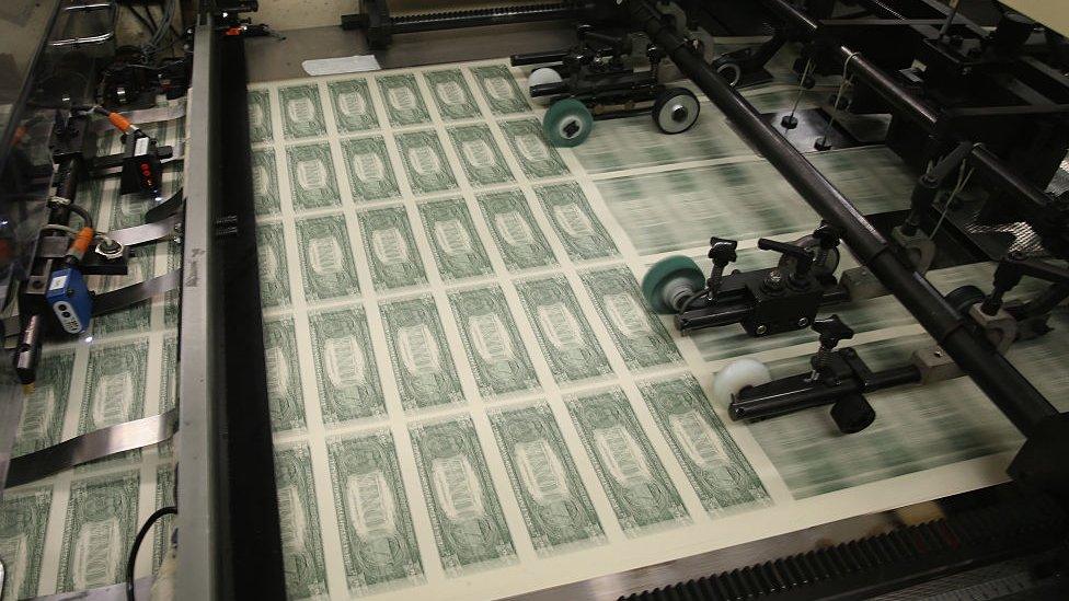 Dollar bills roll off a printing press.