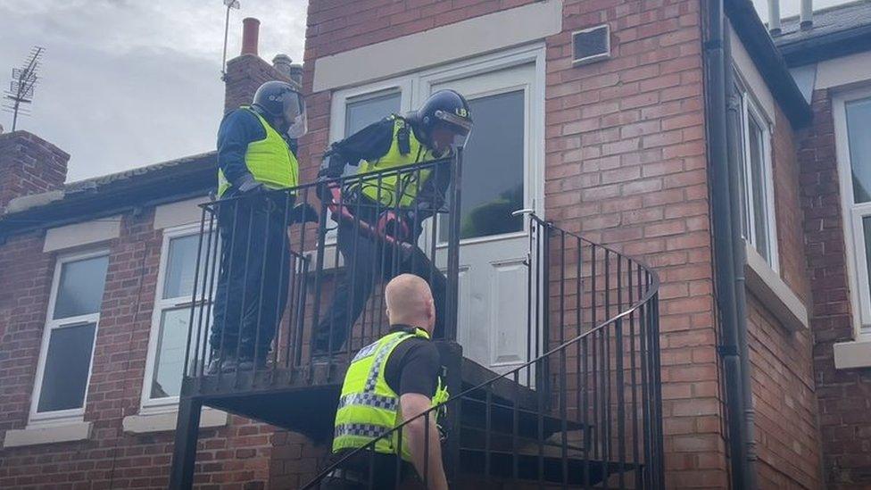 Police in helmets use a metal battering ram to force open a door