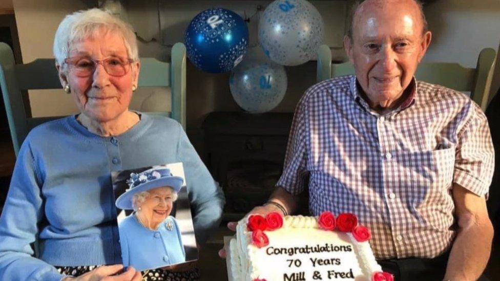 A photo of Fred and Mildred Cosier with their card from the Queen and a cake