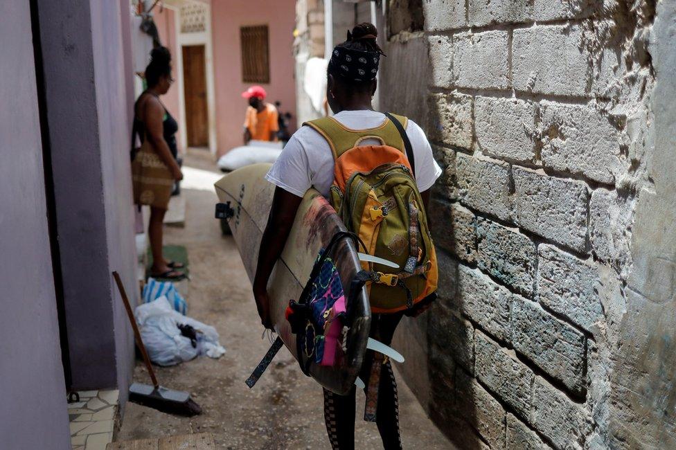 Khadjou Sambe walks down an alleyway holding her surfboard