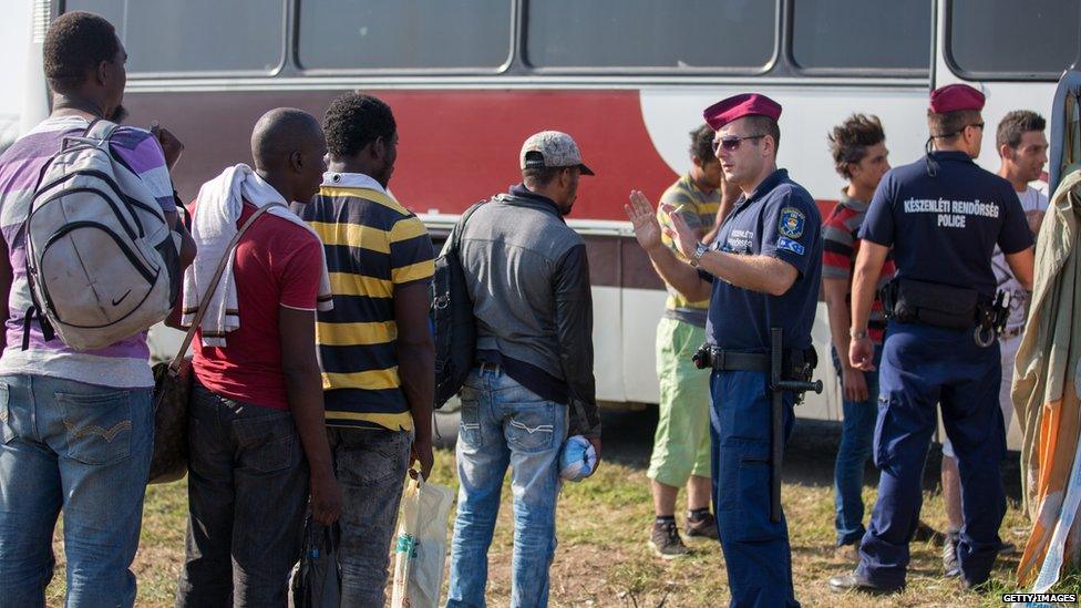 A Hungarian police officer controls a queue of migrants in Szeged, 31 Aug 15