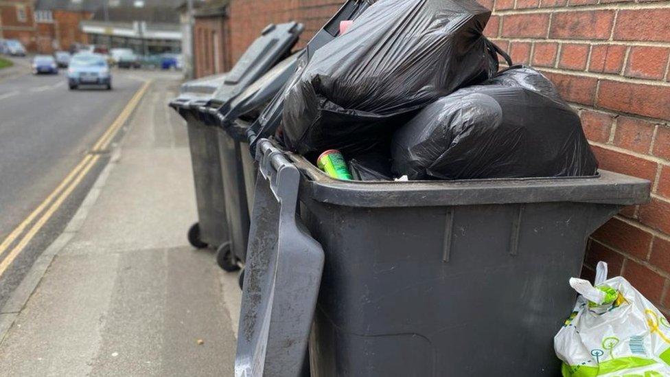 An open black bin with rubbish piled up inside