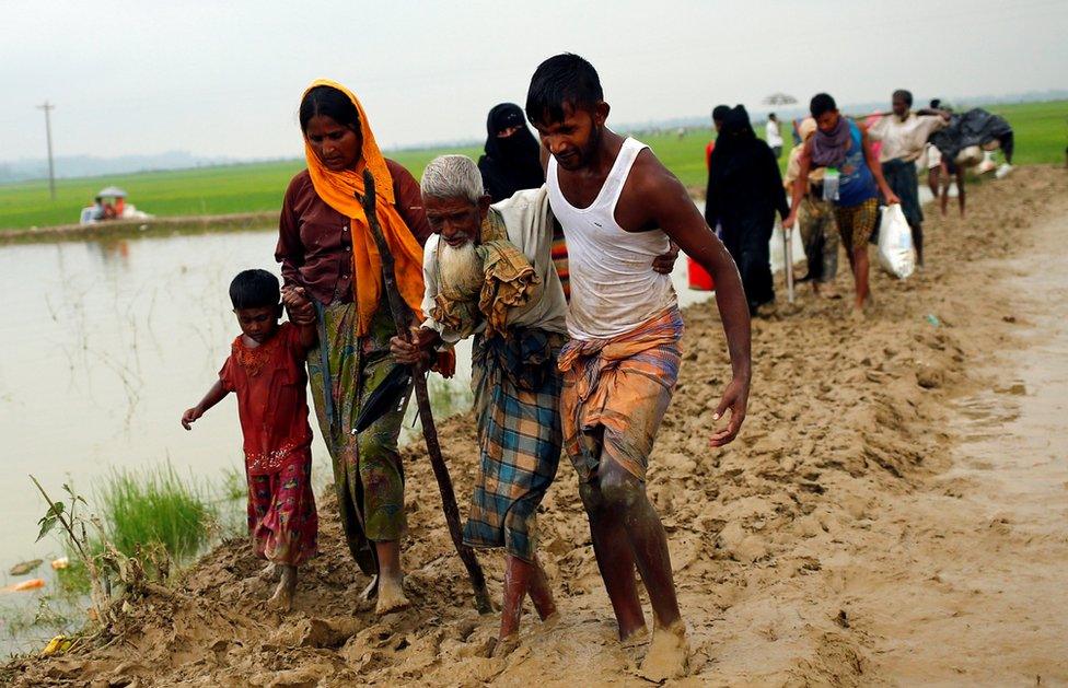 people helping an old man through mud