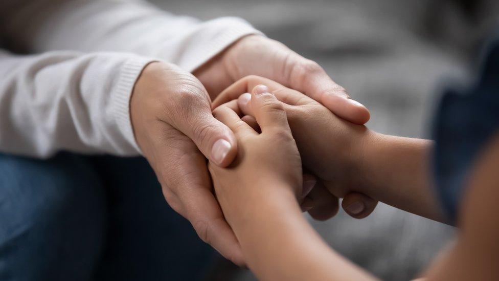 An adult and child holding hands