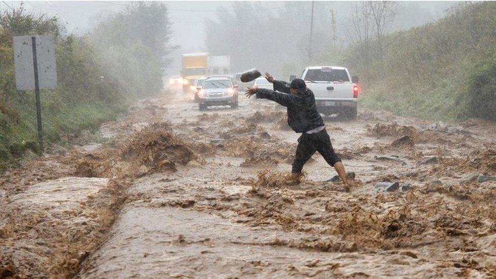 A man helps clear boulders from flooded road as cars negotiate floodwaters caused by Hurricane Helene