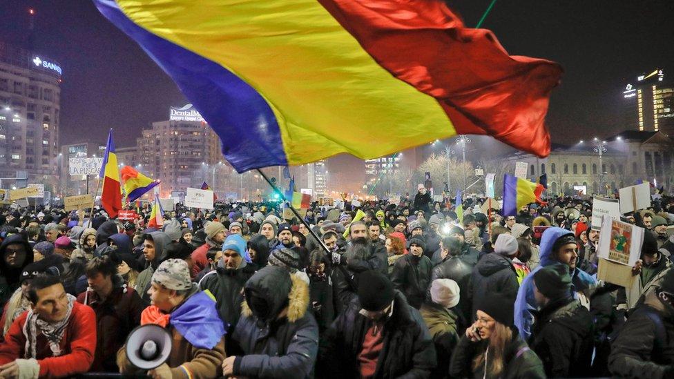 A man waves a large Romanian flag during a protest joined by tens of thousands against a government decree that dilutes what qualifies as corruption, in Bucharest, Romania