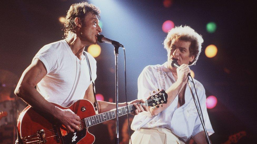 This file photo taken on April 2, 1985 shows French singers Eddy Mitchell (R) and Johnny Hallyday performing at the stadium in Bourges