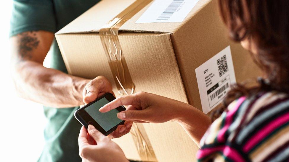 Parcel delivery. A woman can be seen signing a phone, confirming the delivery.