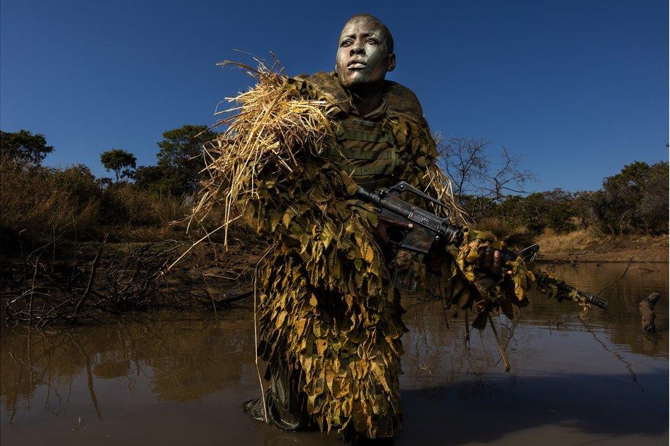 A soldiers stands with a gun wearing camouflage