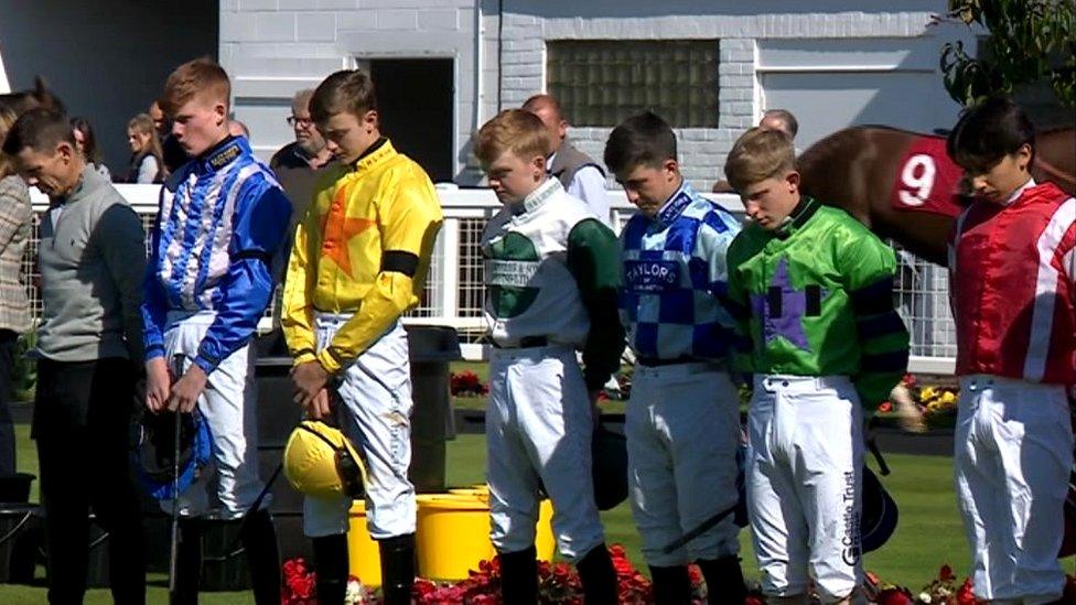 Young jockeys bow their heads during a two minute's silence in memory of the Queen