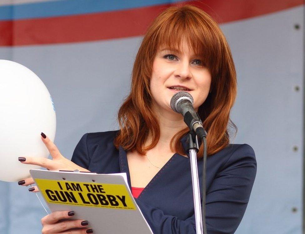 Butina speaks into a microphone while holding a clipboard which says, on its back: I am the gun lobby