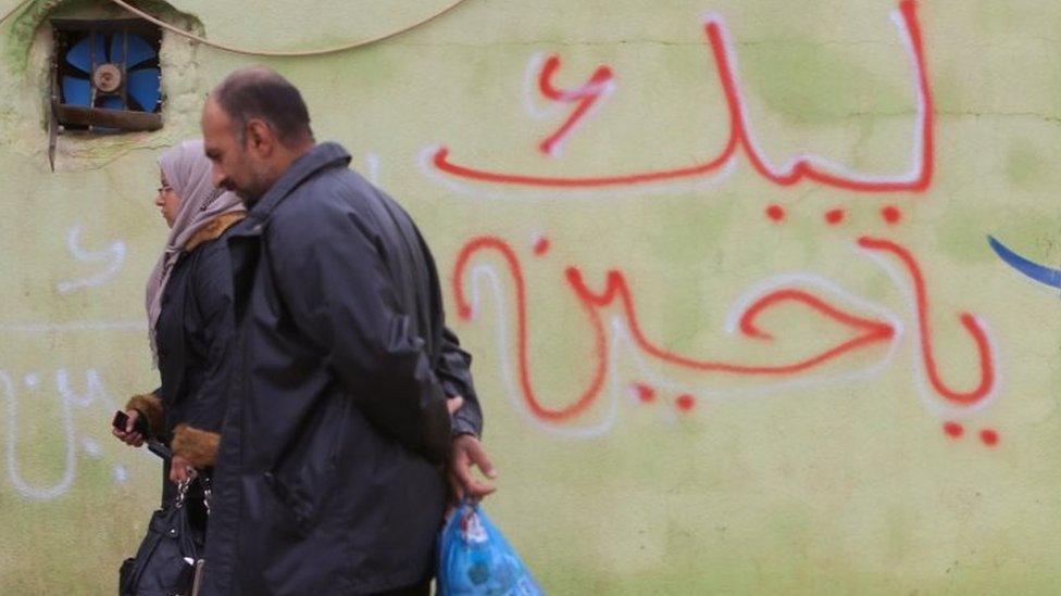 People walk past the slogan "Oh Hussein we are coming" written on a wall in Mosul (02 December 2016)