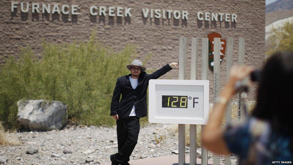 A man stands in front of an unofficial thermometer at Furnace Creek Visitor Center, California.