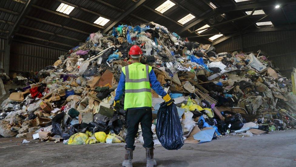 Man standing in front of large pile of rubbish