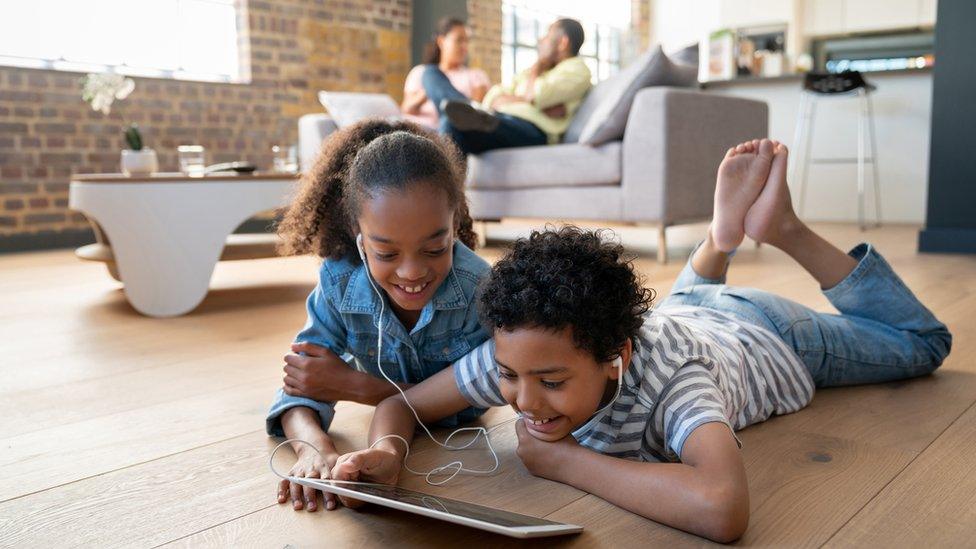 Happy children at home watching videos on a tablet computer using headphones and smiling