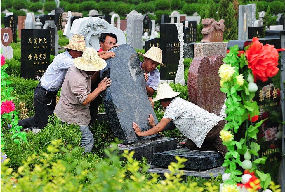 Cemetery workers put a tombstone in place at a cemetery in Tianjin, northern China on 20 July 2010.