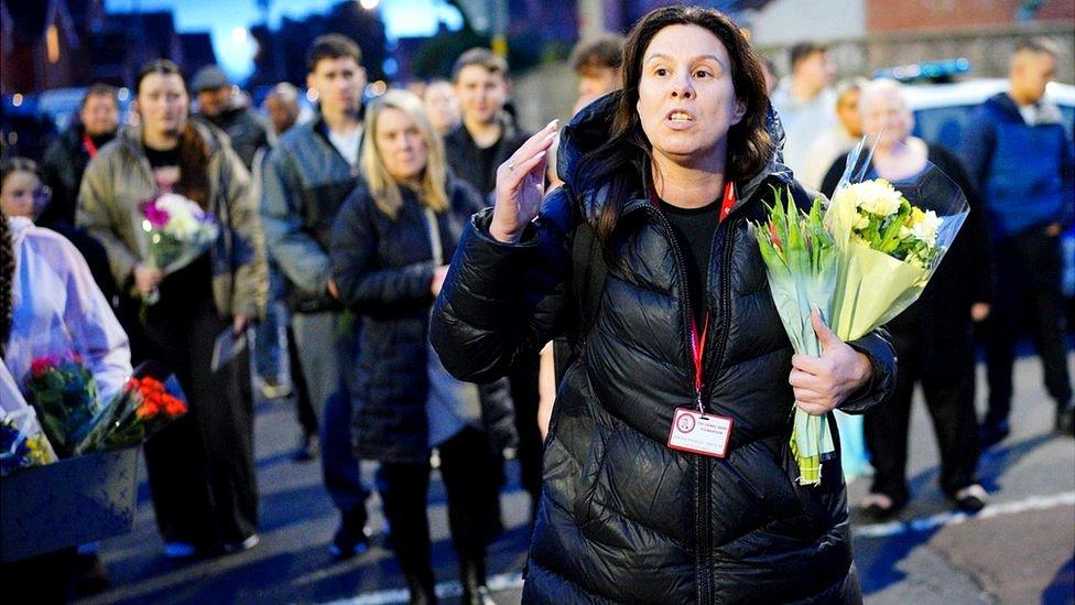 Leanne Reynolds holding flowers talking in a dark puffer jacket