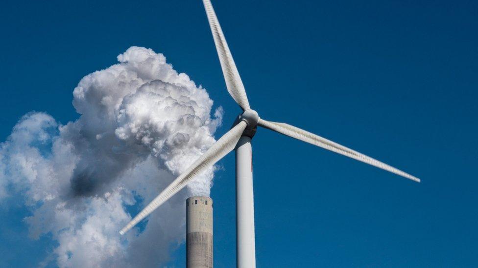 Wind turbine in front of smoking chimney